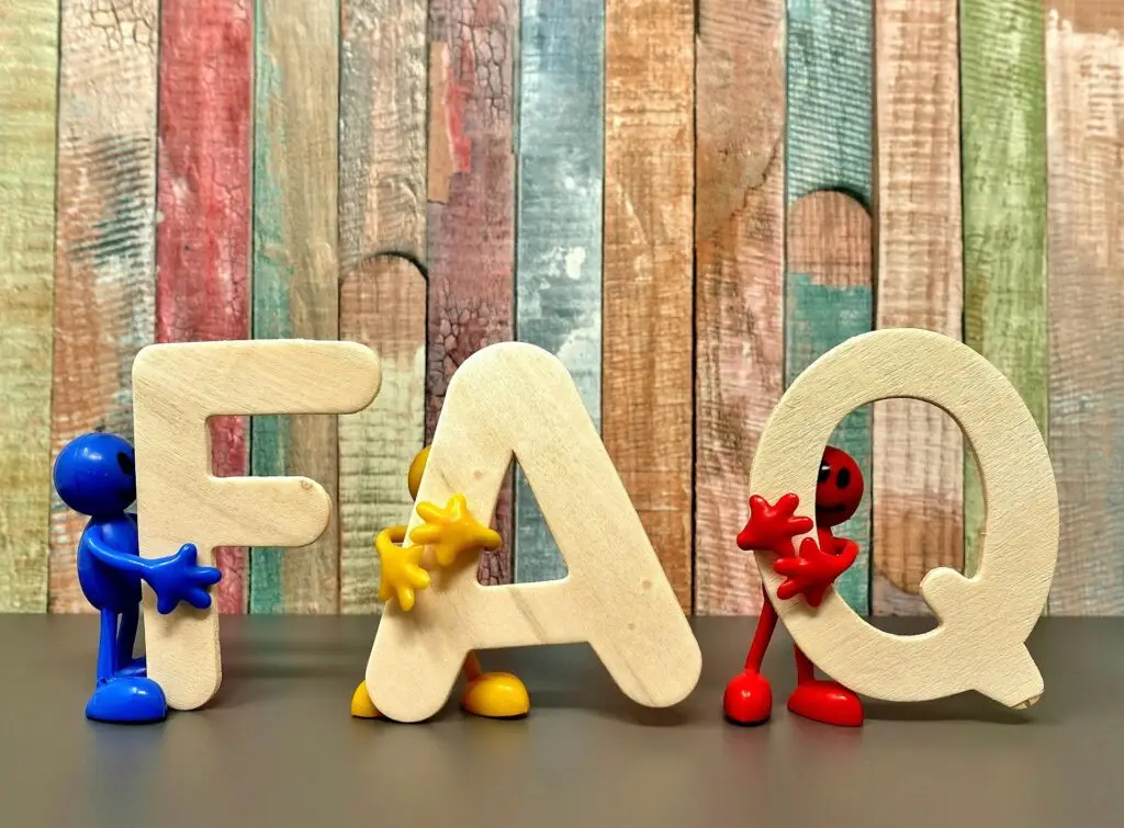 FAQ = Frequently asked questions - image of the three letters in 3D with human-like characters holding them up. Stripy wood wall in background.